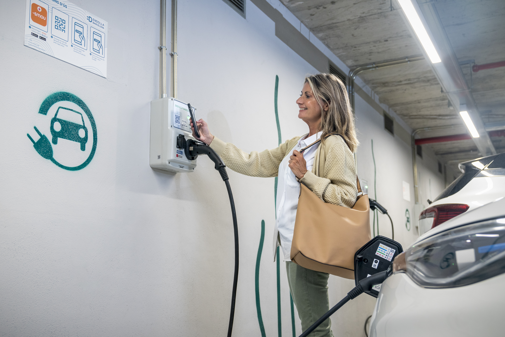 Una mujer carga su vehículo eléctrico en la red Endolla dentro de un Aparcamiento B:SM