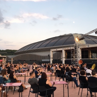 Esplanada de l'Anella Olímpica plena de taules amb assistents i el Palau Sant Jordi de fons