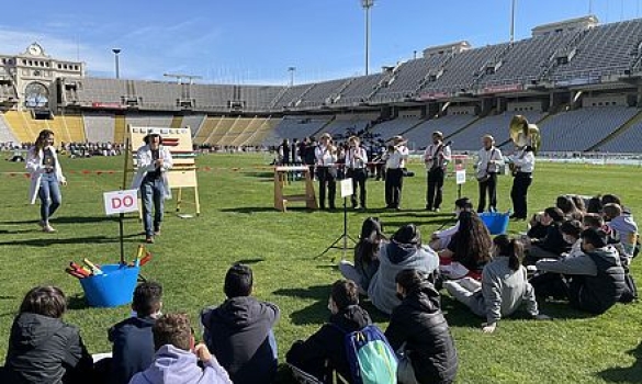 Alumnes sentats a la gespa de l'Estadi Lluís Companys prenent atenció en una de les activitats d'STEAM l'Anella