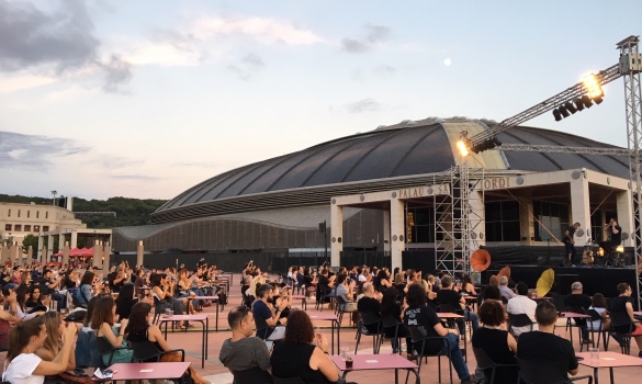 Esplanada de l'Anella Olímpica plena de taules amb assistents i el Palau Sant Jordi de fons
