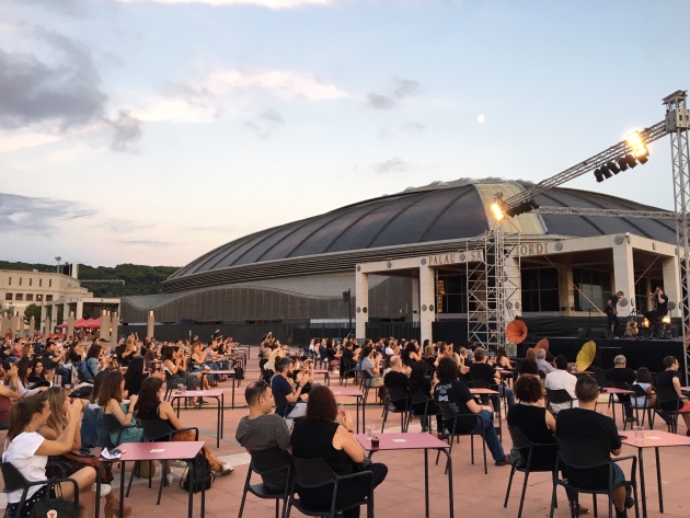 Esplanada de l'Anella Olímpica plena de taules amb assistents i el Palau Sant Jordi de fons